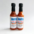 Two bottles of Co>Op Hotsauce Chiracha placed against a white background.